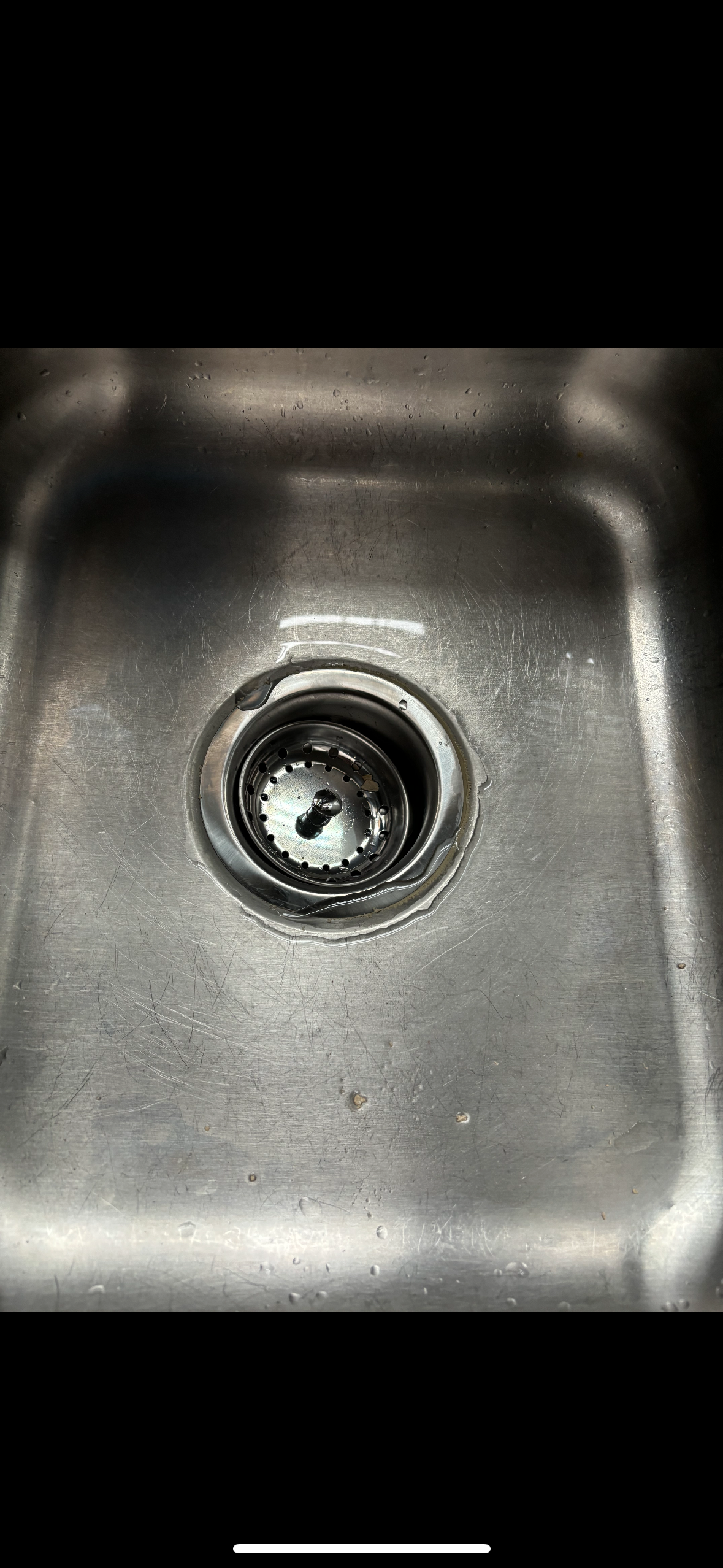 A stainless steel kitchen sink with a metal drain stopper in the center and some water collected around the drain.