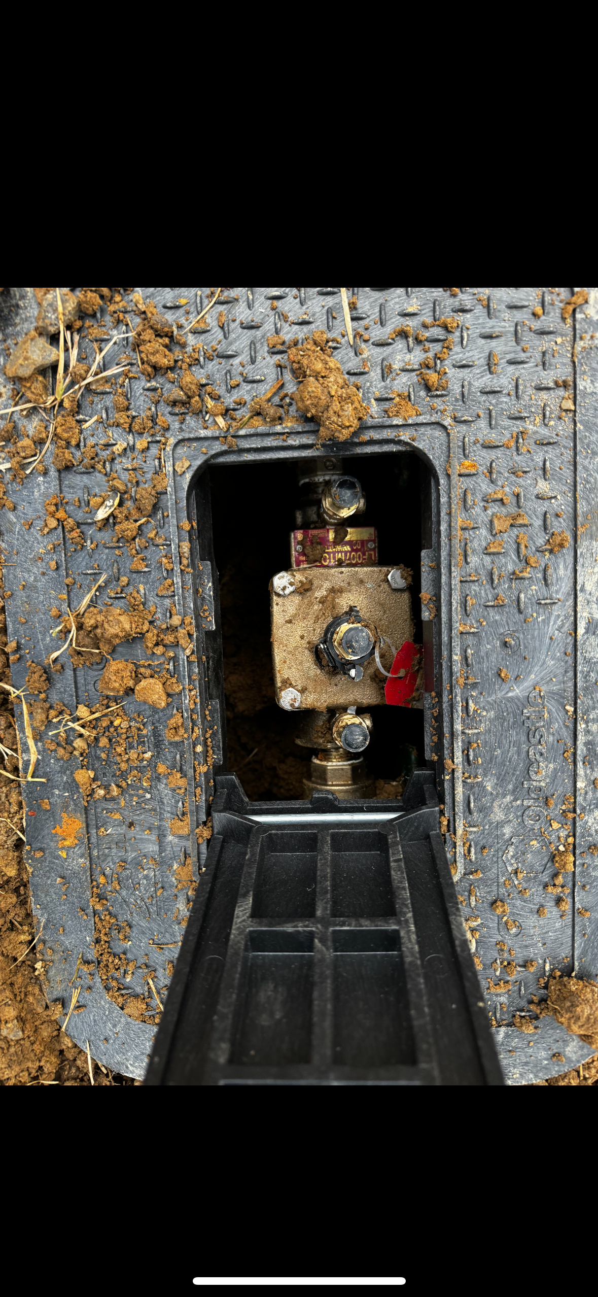 A close-up view of an underground utility box with an exposed brass valve and surrounding dirt.